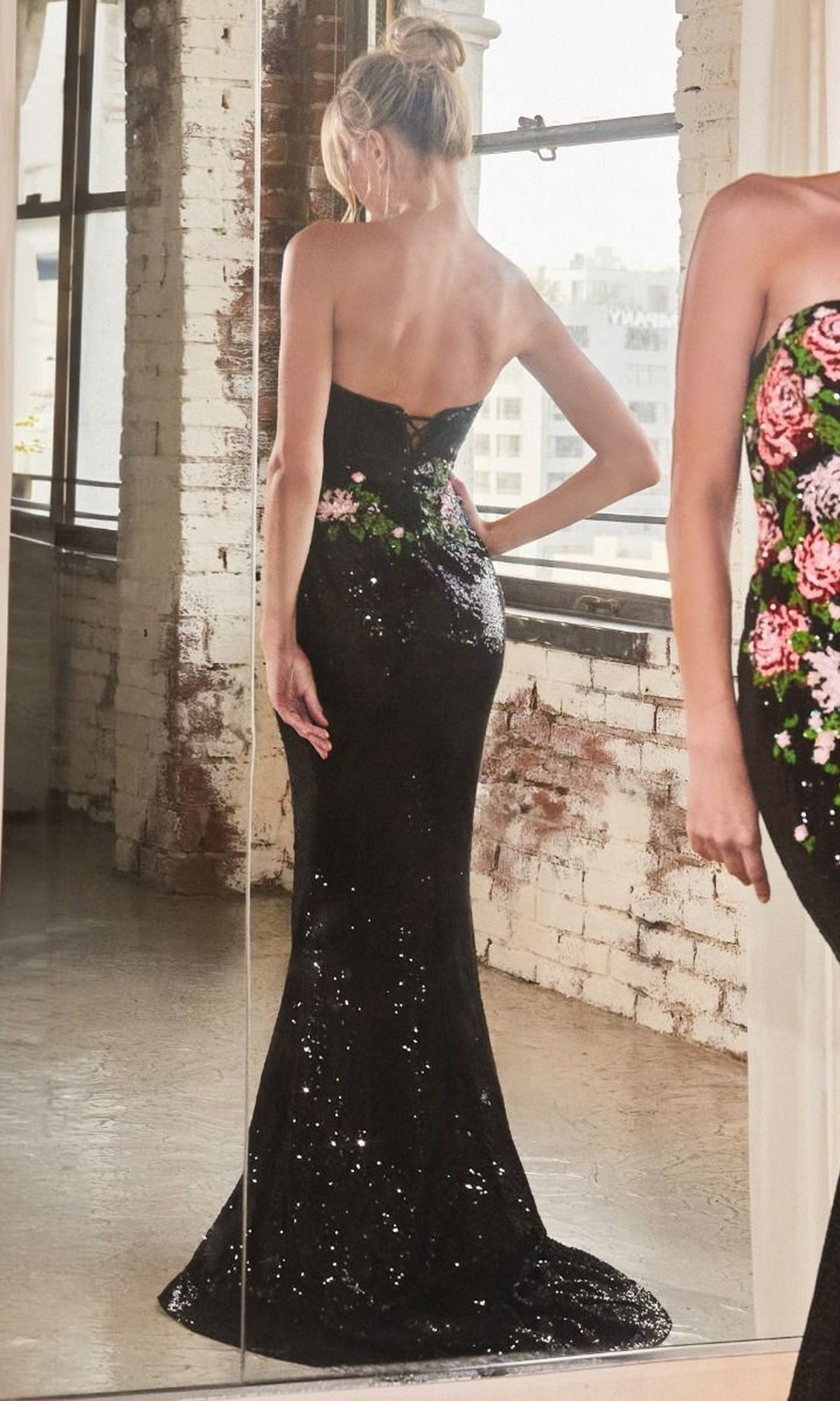 A person stands in front of a mirror wearing the Strapless Long Sequin Floral Formal Dress CD811 in an industrial-style room with white brick walls.